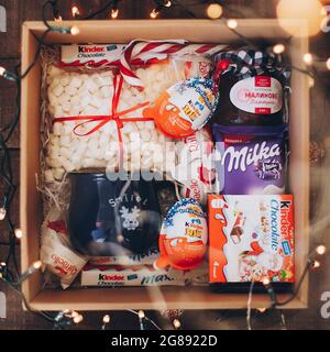 Lviv, Ukraine - December 1, 2017: Homemade jam, marshmallow, cup, raffaello, kinder chocolates in gift box in festive lights. Stylish sweets gift box Stock Photo