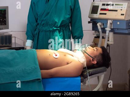 An Asian male patient lies on a bed in the operating room to prepare for treatment by the medical team. Stock Photo