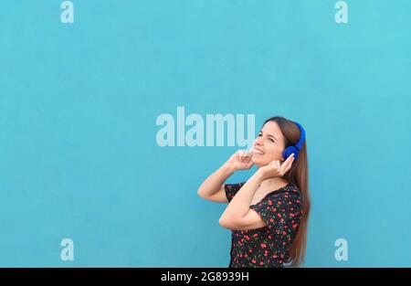 Close up - portrait young beautiful woman in casual outfit wearing headphones standing against a blue background - Summer, joy, relax, concept about g Stock Photo