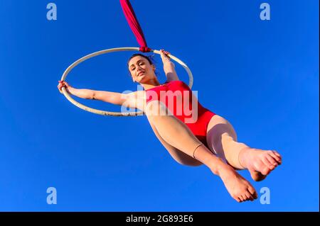 Aerial acrobat in a hoop - Outdoor activity of gymnast performing training on the hoop in the sky - Girl performs the acrobatic elements in the air ri Stock Photo
