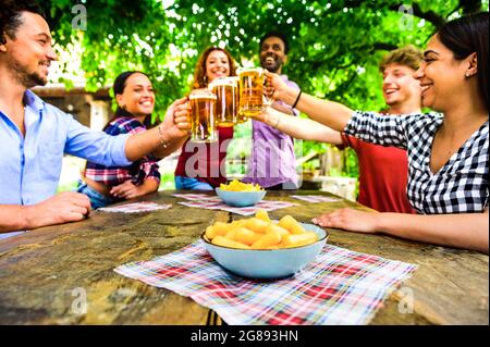 Young multiracial people toasting beer at party - Millennial friends having fun together outside at brewery bar garden on summer - Friendship and happ Stock Photo