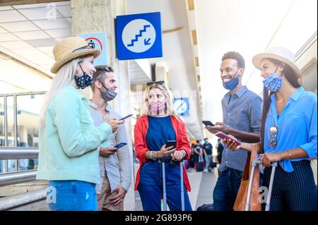 Multiracial friends group having fun with mobile smart phones while waiting for train at railway station - New normal travel concept about young peopl Stock Photo