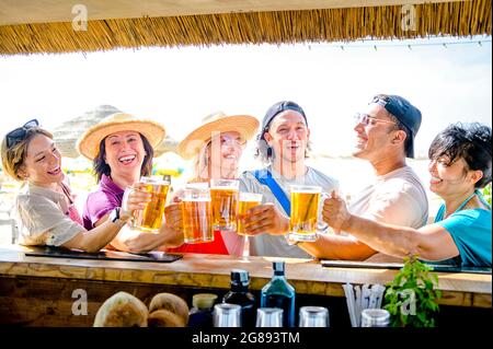 Multiracial friends toasting at beach cocktail bar - Concept  about happy people having fun together cheering beer at summer Stock Photo