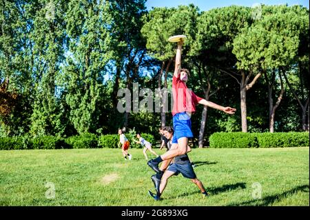 Group of happy friends playing flying disc in the park in summer time - Boy jump for take a frisbie - Sport, education, fun, team, lifestyle concept a Stock Photo