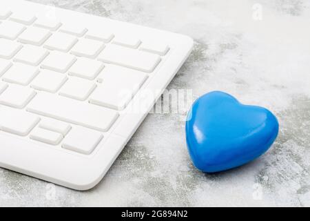Blue heart + white Qwerty keyboard for Blue Monday, feeling gloomy / dispirited, poor office morale, being dumped online, Covid lockdown mental blues. Stock Photo