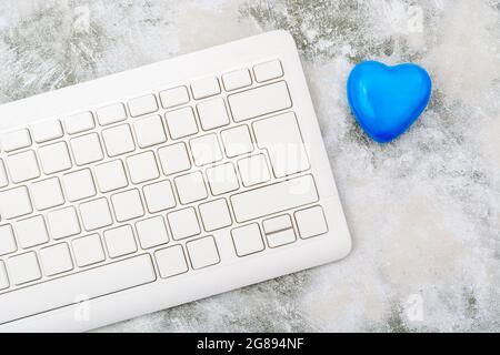 Blue heart + white Qwerty keyboard for Blue Monday, feeling gloomy / dispirited, poor office morale, being dumped online, Covid lockdown mental blues. Stock Photo