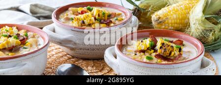 Narrow view of three bowls of chicken and corn chowder topped with grilled corn and bacon, ready for eating. Stock Photo