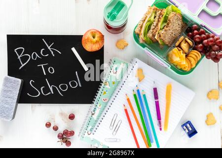 Top down view of various school supplies, a lunch kit and a black chalkboard with the words Back to School written on it Stock Photo