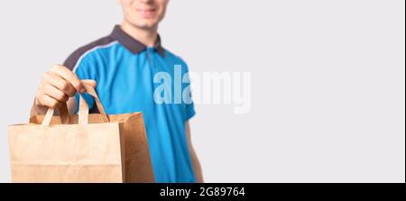 Delivery man in a blue polo shirt holding a package carton bag with handless pulling it forward and smiling. Stock Photo