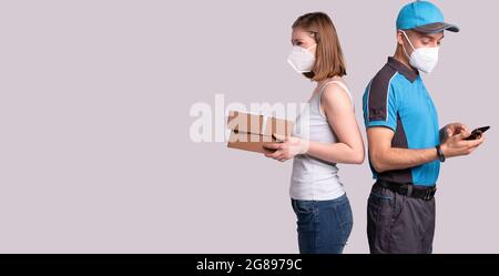 Nice woman got the parcel on pandemic time so she is standing back to back with courier and they both in medical mask. Stock Photo