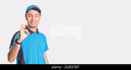 Photo of a smiling delivery man standing in front of camera showing with the gesture everything is fine and winking. Stock Photo