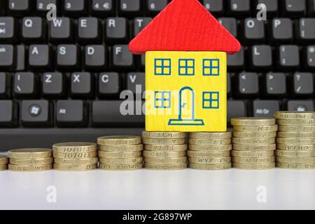 A toy house on a rising stack of coins with a computer keyboard, to symbolise searching for houses online. Stock Photo