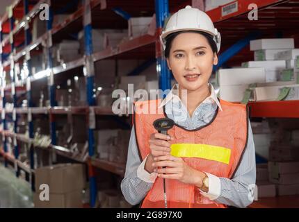 Portrait of a confident female warehouse worker in uniform holding a product scanner within the working environment inside the warehouse. Stock Photo