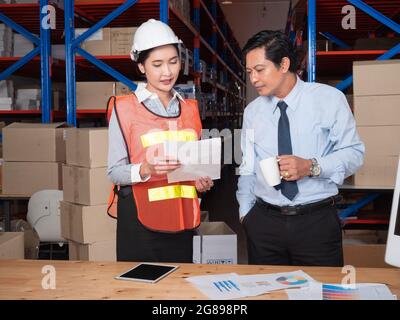 An Asian male warehouse manager, while in a good mood, explaining the volume of delivery to the customer to the warehouse operator. wholesale, logisti Stock Photo