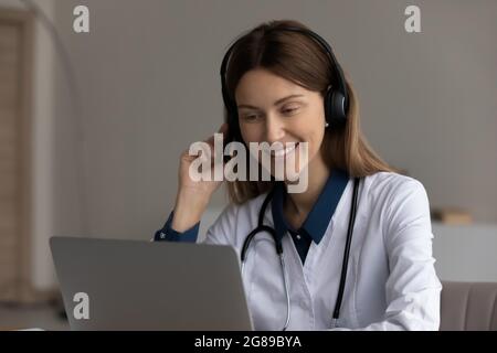 Happy friendly female doctor in headset using laptop Stock Photo