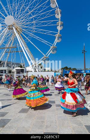 Bournemouth, Dorset, UK. 18th July, 2021. Afon Sistema with their whirling dancers with colourful skirts play Maracatu, Samba's earthier cousin from Northeastern Brazilas perform as part of the Arts by the Sea Summer Series on a hot sunny crowded day at the seaside. Credit: Carolyn Jenkins/Alamy Live News