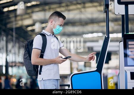 Man using self service check-in machine. Passenger scanning ticket on smart phone at airport terminal. Stock Photo