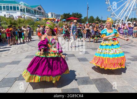 Bournemouth, Dorset, UK. 18th July, 2021. Afon Sistema with their whirling dancers with colourful skirts play Maracatu, Samba's earthier cousin from Northeastern Brazilas perform as part of the Arts by the Sea Summer Series on a hot sunny crowded day at the seaside. Credit: Carolyn Jenkins/Alamy Live News