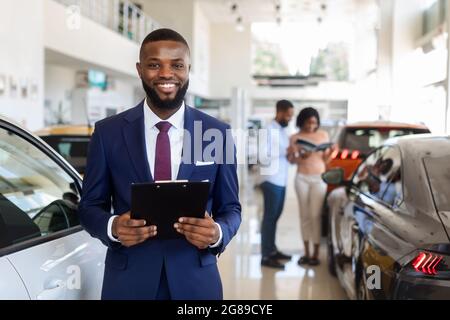 Handsome Black Car Salesman In Suit Posing At Workplace In Auto Showroom Stock Photo