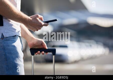 Man holding smartphone and using mobile app against a row of taxi cars. Themes modern technology, carsharing and travel. Stock Photo