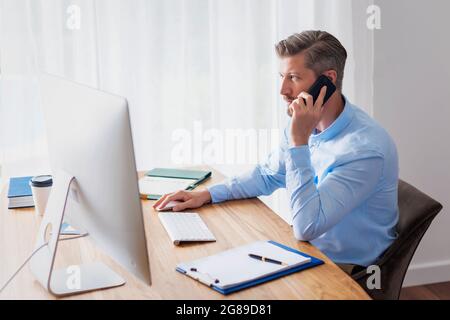 Businessman sitting at desk behind his computer and having a phone call. Home office. Stock Photo