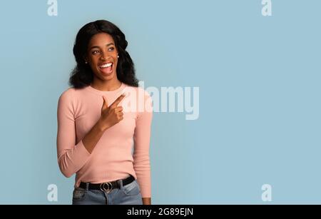 Great Offer. Cheerful Young African American Woman Pointing Finger And Looking Aside Stock Photo