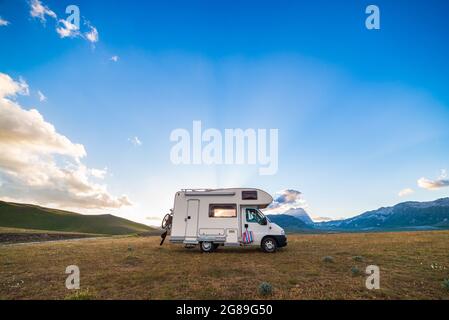 Sunset dramatic sky over camper van in Campo Imperatore highlands, Abruzzo, Italy. Epic clouds above unique highlands and rocky mountains landscape, a Stock Photo