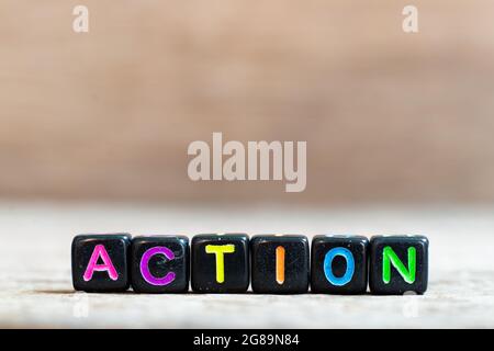 Black bead with color alphabet in word action on wood background Stock Photo