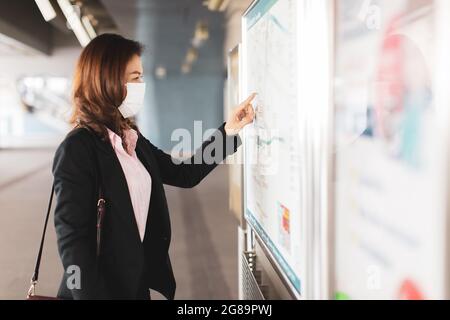 Beautiful Asian woman in a black suit wearing medical hygiene protective mask standing and looking to read map at Skytrain station. Concept for worker Stock Photo