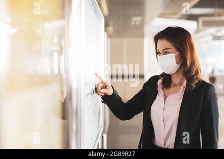 Beautiful Asian woman in a black suit wearing medical hygiene protective mask standing and looking to read map at Skytrain station. Concept for worker Stock Photo