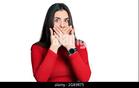 Young brunette teenager wearing red turtleneck sweater shocked covering mouth with hands for mistake. secret concept. Stock Photo