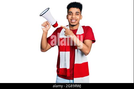 Young african american man football hooligan holding megaphone smiling happy pointing with hand and finger Stock Photo