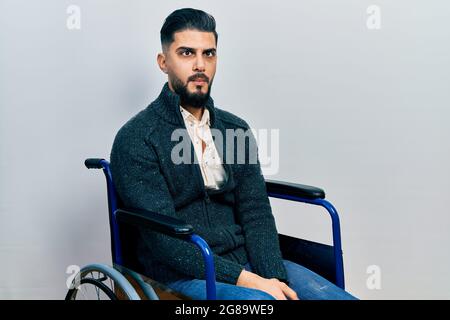 Handsome man with beard sitting on wheelchair making fish face with lips, crazy and comical gesture. funny expression. Stock Photo