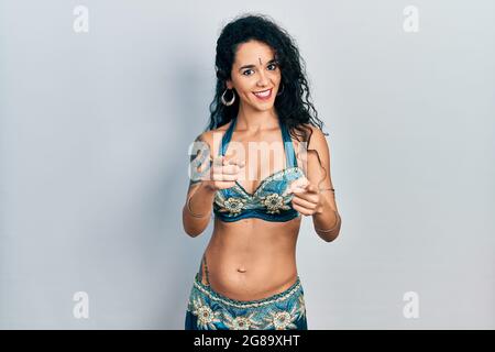 Young woman wearing bindi and traditional belly dance clothes pointing fingers to camera with happy and funny face. good energy and vibes. Stock Photo
