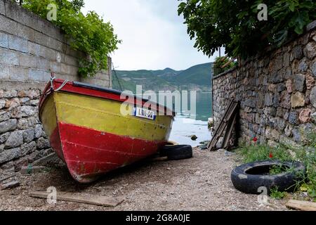 Traditional red and yellow albanian fishing boa moored on shore of Lake Ohrid by the houses in the village of Lin, Albania Stock Photo