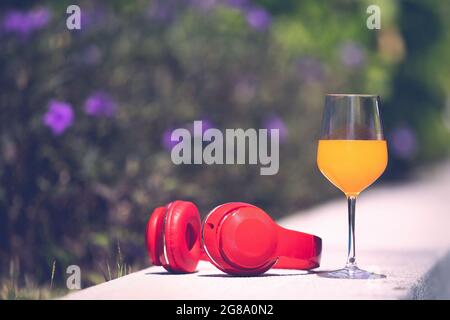 Glass of orange juice and red headphone on edge of swimming pool with blur flower and green tree in background. Copyspace on the left, process in vint Stock Photo