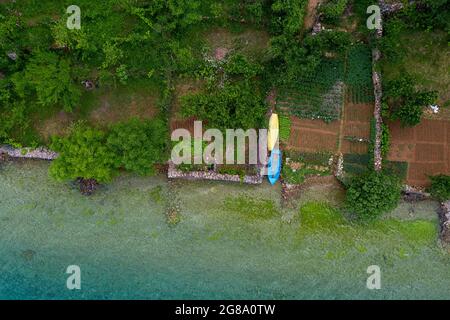 Aerial view of traditional albanian fishing boats moored by vegetable garden on shore of Lake Ohrid surrounding Lin Peninsula, Albania, taken by drone Stock Photo