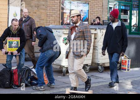 London, UK - November 2019, A fashionable man in a cap and plaid jacket walks past a protesting man holding a poster - fur kills - at a Sunday street Stock Photo