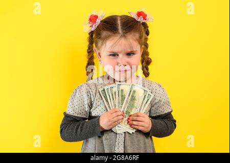 Children and financial responsibility, little girl on a yellow background with dollars in her hands, financial literacy in a child. Stock Photo