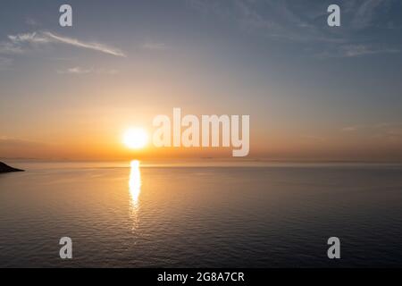 Sunset orange color over calm sea water. Dramatic magical sunrise seascape in Aegean sea, Greece. Golden reflections on the rippled water. Cyclades is Stock Photo