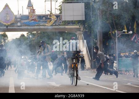 A protester rides a bicycle amidst tear gas smoke during the demonstration.The Anti-government group rally gathered at the Democracy Monument and proceeded to the Thai Government House, in response to a week of daily new highs in death toll and patients record soaring to more than 10,000 per day. The protesters demanded the resignation of Prime Minister Prayut Chan-ocha and his cabinet, defying the government's ban on public gatherings. The riot police began firing the water cannon and massive amount of tear gas was used to crackdown a protest. Stock Photo