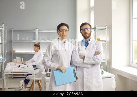 Portrait of scientists in lab coats and goggles standing in modern medical laboratory Stock Photo