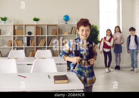 Smiling caucasian schoolboy with backpack stand next to desk posing for camera Stock Photo
