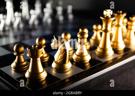 A horizontal shot of cool gold chess pieces in the starting position reflected on the board Stock Photo