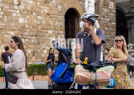 Man tourist with a bike next to Uffizi museum and David sculpture, wearing face masks during covid 19 quarantine in Italy. Slow reopening Stock Photo