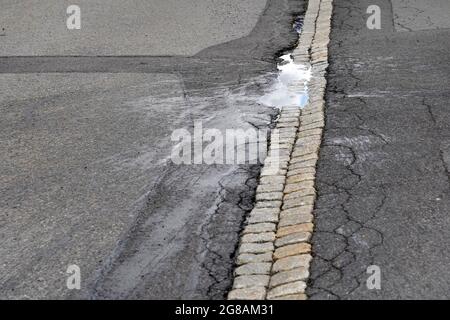 Road with a pothole. There is a puddle of rain water in the pothole. The water is splashed around as well. In the puddle there is reflection of the sk Stock Photo
