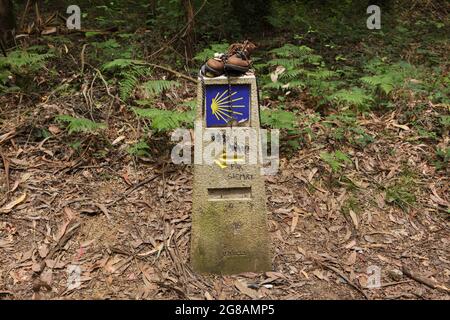 Camino de Santiago (Way of Saint James). Pilgrim boots placed on the traditional kilometre milestone of the Camino de Santiago near the town of Arzúa in Galicia, Spain. The French route and the Northern route of the Camino de Santiago go through this town shortly before both routs reach Santiago de Compostela. The scallop shell, also known as the Shell of Saint James is depicted in the milestone as a traditional symbol of the pilgrimage to Santiago de Compostela. Stock Photo