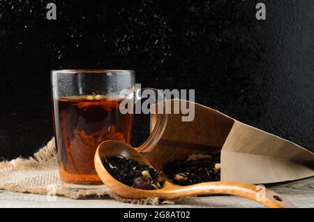 A glass mug of fragrant brewed flower tea on a wooden table, with a wooden spoon and tea leaves in a paper bag. Selective focus. Stock Photo