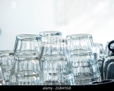 Close up upside down empty drinking water glasses. Stacks of clean and dried empty glass on white wall background in cafe. Stock Photo
