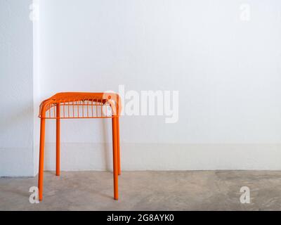Empty DIY chair orange color made from steel and wire on concrete floor and white wall background with copy space. Modern chair with geometric grid wi Stock Photo